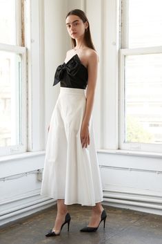 a woman standing in front of a window wearing a black and white dress with a bow at the waist