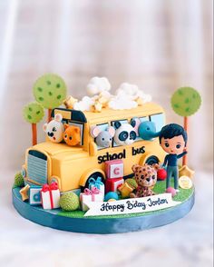 a school bus cake is decorated with animals and presents on the front, as well as an image of a boy holding a teddy