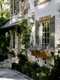 a white house with green shutters and flowers in the window boxes on the side