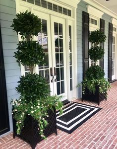 two black planters with white flowers are on the front porch