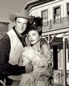 an old black and white photo of two people in front of a house with a cowboy hat on