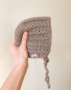 a hand holding up a crocheted hat on top of a white wall