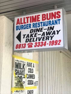 a restaurant sign hanging from the side of a building next to a wall with posters on it