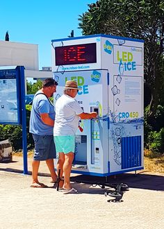 two men standing in front of a large machine with an electronic clock on it's side