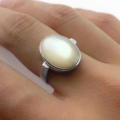 "This is a handmade ring of a large lustrous oval Mother of Pearl. When the stone catches the light it displays a brilliant iridescent glow! The contemporary silhouette of the curved ring band allows the gemstone to truly shine. Available in sizes 5-12. Custom sizing is available upon request!  Dimensions: The hand model is wearing a size 7. The stone measures 16x12mm (about 3/4\" inch). The band is 3mm wide, and the entire face of ring is 17mm, or almost 3/4\" inches. The bezel around the stone Modern Oval Cabochon Moonstone Ring, Modern Oval Moonstone Ring With Large Stone, Modern Oval Cabochon Opal Ring As Gift, Handmade Oval Moonstone Ring In Modern Style, Handmade Modern Oval Moonstone Ring, Modern Handmade Oval Moonstone Ring, Classic Oval Rings With High Luster, Classic Oval Ring With High Luster, Modern Oval Pearl Ring For Anniversary