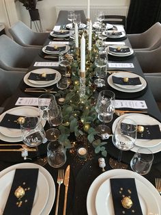 the table is set with black and white plates, silverware, candlesticks and greenery