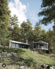 a house in the woods surrounded by trees and rocks on a hill with an overhang