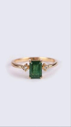 a gold ring with an emerald stone and two diamonds on the band, set against a white background