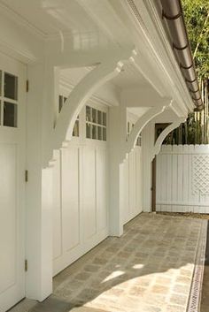 a white house with an arched roof and wooden doors on both sides, in front of a white picket fence