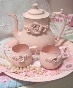 a pink tea set sitting on top of a table next to a white plate with two cups and saucers