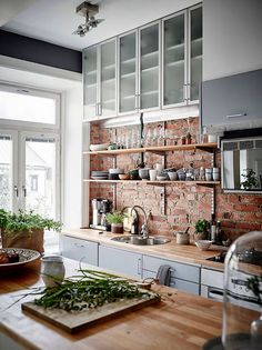 a kitchen with brick wall and wooden counter tops, plants on the shelf above the sink