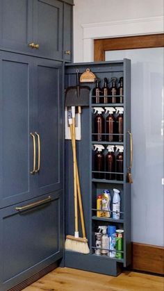 an open cabinet in the corner of a kitchen with brooms and cleaning products on it