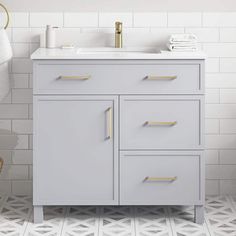 a bathroom vanity with white tile and gold handles on the drawers, along with a towel rack