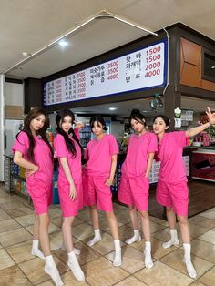 four women in pink outfits standing next to each other and pointing at an electronic sign