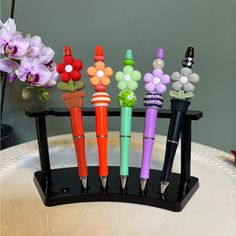 several pens are lined up in a holder with flowers on them and beads attached to the ends