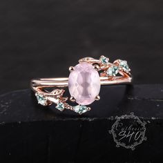 a ring with an oval pink stone surrounded by green and white stones on top of a black surface