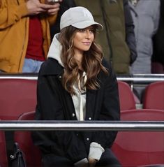 a woman sitting in the stands at a baseball game wearing a white hat and black jacket