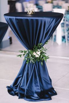 the table is covered with blue cloth and has an arrangement of greenery on it