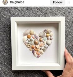 a hand holding up a white frame with seashells in the shape of a heart