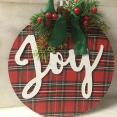 a christmas ornament hanging on the side of a wall with holly and pine cones