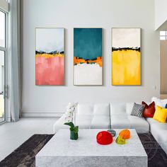 three abstract paintings hang on the wall above a white couch and coffee table in a modern living room