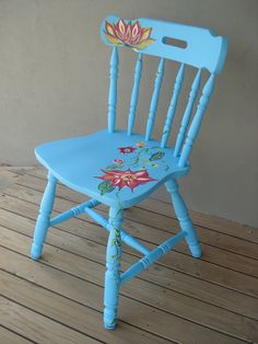 a blue wooden chair with flowers painted on the back and seat, sitting on a wood floor