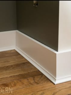 the corner of a room with wood flooring and white trim on the bottom part of the wall