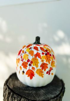 a painted pumpkin sitting on top of a piece of wood with leaves all over it