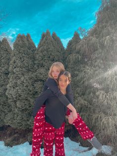 two women hugging each other in front of trees and snow covered ground with blue sky