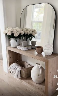 a wooden shelf with vases and flowers on it next to a mirror in a room