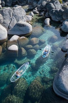 two people in kayaks paddling on clear water near large rocks and rock formations