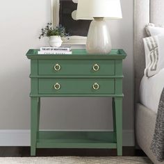 a green table with two drawers and a lamp on it next to a white bed