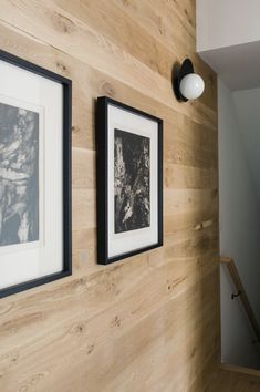 two framed photographs hang on the wall next to a stair case with wood paneling