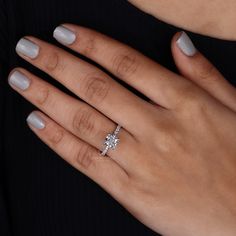 a woman's hand with a diamond ring on her left hand and grey manicured nails