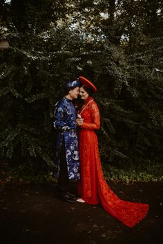 a man and woman dressed in traditional chinese clothing standing next to each other with trees behind them