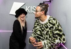 two people standing next to each other in front of a kiis sign and smiling