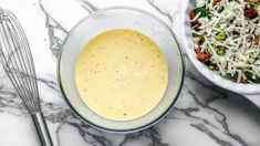 two bowls filled with different types of food on top of a marble counter next to a whisk