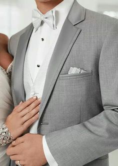 a man in a gray suit and bow tie standing next to a woman wearing a white dress