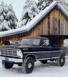 an old black truck parked in front of a wooden building with snow on the ground