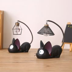 two cat figurines sitting on top of a table next to a light bulb