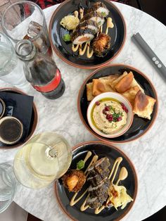 three plates with different types of food on top of a white marble table next to wine glasses and utensils