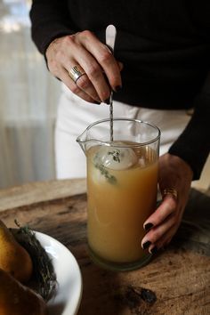 a person is pouring something into a glass on a table with pears and other fruit