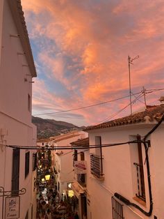 the sky is pink and orange as people walk down an alleyway at sunset or dawn