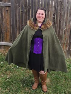 a woman wearing a cape and boots standing in the grass