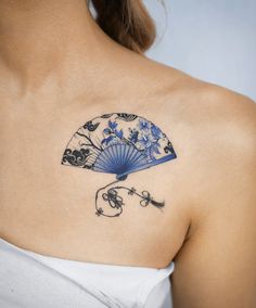 a woman with a tattoo on her shoulder holding a blue fan and skulles in front of her back