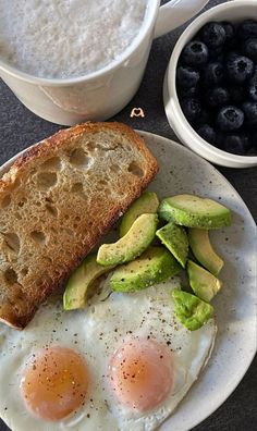 two eggs and toast on a plate with blueberries, avocado and yogurt