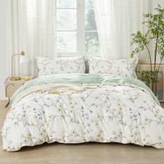 a bed with white and green comforters in front of a window, next to a potted plant