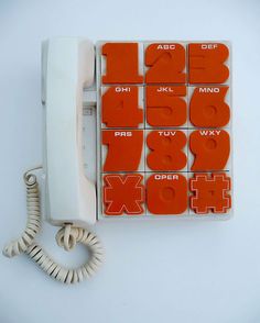 an orange and white phone sitting on top of a table next to a telephone cord