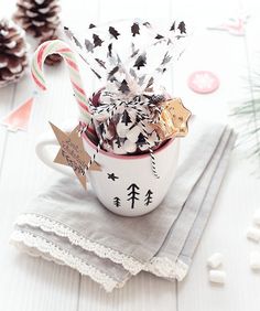 a cup filled with candy canes on top of a napkin next to pine cones