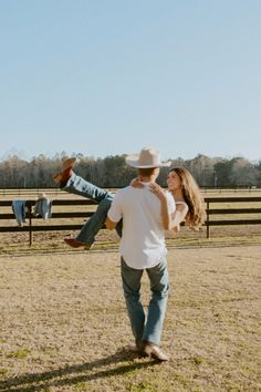 a man holding a woman in the air while standing next to a fence and wearing a cowboy hat